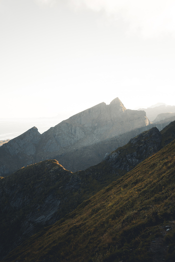 View of the rugged peaks of Reinebringen mountain illuminated by golden hour light with dramatic shadows and grassy slopes in Moskenes Nordland Norway.
