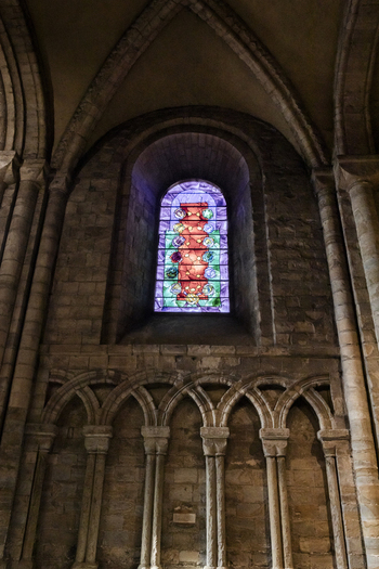 View of the colorful stained glass window set within the historic Romanesque stone arches of Durham Cathedral in Durham England United Kingdom. View of the colorful stained glass window set within the historic Romanesque stone arches of Durham Cathedral in Durham England United Kingdom.