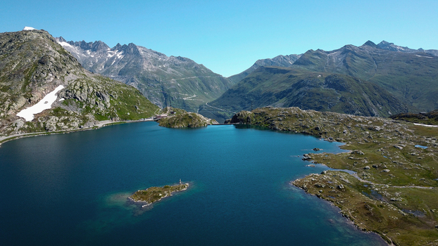 Aerial view of the deep blue waters of Totensee at Grimsel Pass surrounded by rugged alpine peaks and winding mountain roads under a clear sky in Obergoms Valais Switzerland. Aerial view of the deep blue waters of Totensee at Grimsel Pass surrounded by rugged alpine peaks and winding mountain roads under a clear sky in Obergoms Valais Switzerland.