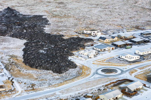 Aerial view of stark black hardened lava flow encroaching on a snow dusted town a dramatic contrast of destruction and resilience Grindavik Grindav&iacute;kurb&aelig;r Iceland.