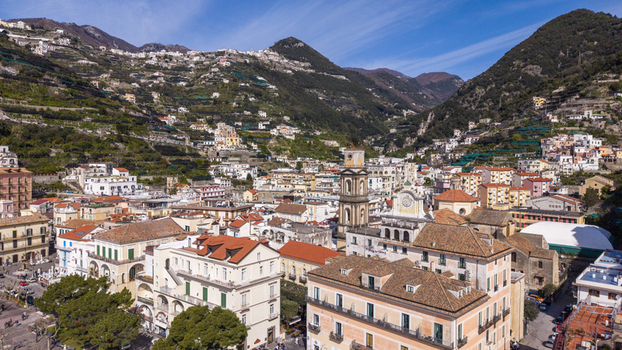 Aerial view of sun kissed buildings with terracotta roofs cascade down the slopes towards the town square nestled against the majestic mountains Minori Campania Italy. Aerial view of sun kissed buildings with terracotta roofs cascade down the slopes towards the town square nestled against the majestic mountains Minori Campania Italy.