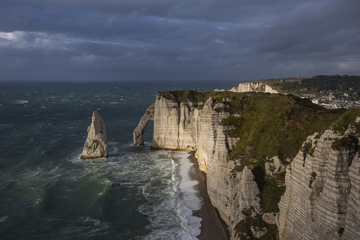 Aerial view of dramatic white cliffs meeting the turbulent sea under a brooding sky showcasing the iconic arch of &Eacute;tretat &Eacute;tretat France.