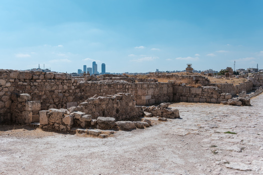 View of the historic stone ruins of the Umayyad Palace with the modern skyline of the city in the background under a clear blue sky in Amman Amman Governorate Jordan.