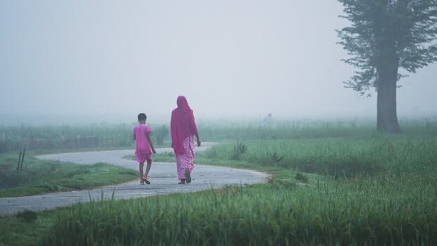 View of a woman and child walking on a path in the fog Bangladesh.