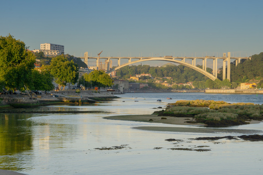 View of tranquil waters reflecting the morning light framed by lush greenery and the iconic Arrábida Bridge stretching across the Douro River Porto Portugal. View of tranquil waters reflecting the morning light framed by lush greenery and the iconic Arrábida Bridge stretching across the Douro River Porto Portugal.