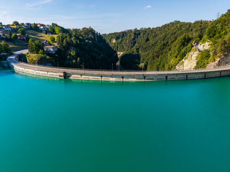 Aerial view of Barrage de Rossens holding back the turquoise waters of Lac de la Gruyere surrounded by lush green hills and residential houses in Pont la Ville Fribourg Switzerland.