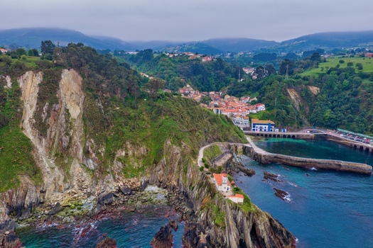 Aerial view of the historic town of Cudillero and its lighthouse perched on steep cliffs overlooking the harbor and misty green hills in Cudillero Asturias Spain. Aerial view of the historic town of Cudillero and its lighthouse perched on steep cliffs overlooking the harbor and misty green hills in Cudillero Asturias Spain.