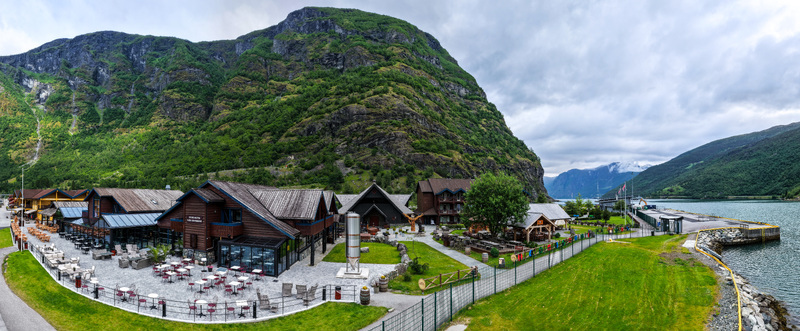 Aerial view of the waterfront area in Flam featuring wooden buildings outdoor restaurant seating and a brewery set against lush green mountains and the fjord Flam Vestland Norway. Aerial view of the waterfront area in Flam featuring wooden buildings outdoor restaurant seating and a brewery set against lush green mountains and the fjord Flam Vestland Norway.