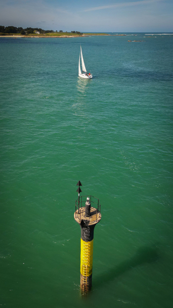 Aerial view of a solitary sailboat glides across the tranquil turquoise waters near a channel marker Roscoff Brittany France. Aerial view of a solitary sailboat glides across the tranquil turquoise waters near a channel marker Roscoff Brittany France.