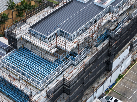 Aerial view of a building under construction featuring steel framing and extensive scaffolding covered in black safety netting in Melbourne VIC Australia.