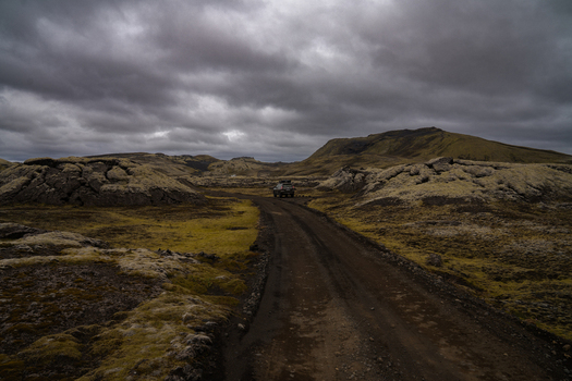 View of a lone vehicle traverses a rugged dirt road through a desolate moss covered landscape under a dramatic brooding sky Skaftárhreppur Iceland. View of a lone vehicle traverses a rugged dirt road through a desolate moss covered landscape under a dramatic brooding sky Skaftárhreppur Iceland.
