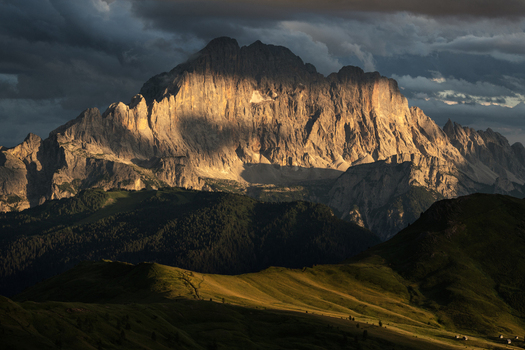 View of Dolomites mountain peaks illuminated by golden sunset light under dramatic storm clouds and green hills Trentino Alto Adige Italy. View of Dolomites mountain peaks illuminated by golden sunset light under dramatic storm clouds and green hills Trentino Alto Adige Italy.