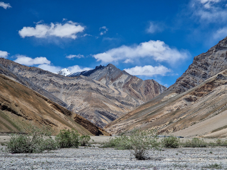 View of the rugged mountain landscape near the Penzi La road with rocky terrain sparse shrubs and snow capped peaks under a blue sky in Zanskar Ladakh India.