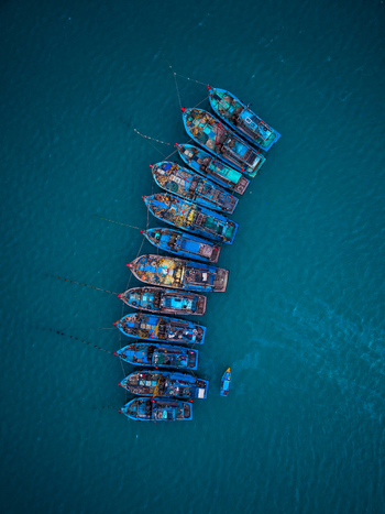Aerial view of a line of traditional wooden fishing boats moored in deep blue water in Vietnam. Aerial view of a line of traditional wooden fishing boats moored in deep blue water in Vietnam.