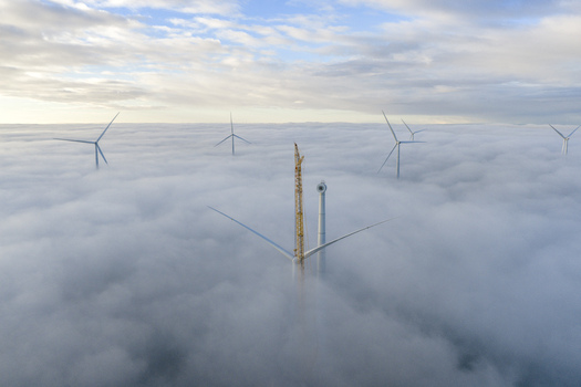 Aerial view of wind turbines and a construction crane rising above a thick blanket of clouds under an overcast sky Netherlands. Aerial view of wind turbines and a construction crane rising above a thick blanket of clouds under an overcast sky Netherlands.