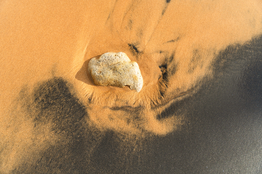 View of a porous rock resting on contrasting golden and black volcanic sand on a beach in Galle Southern Province Sri Lanka.