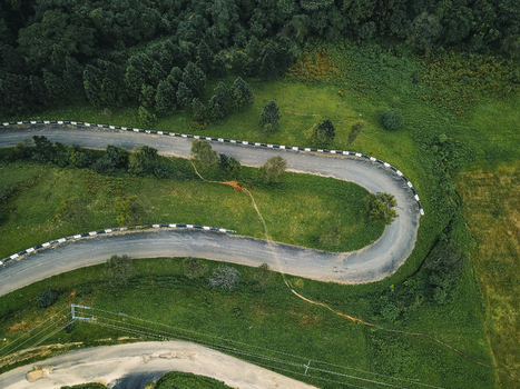 Aerial view of a winding asphalt road its stark grey contrasting with vibrant emerald forests and lush green hills Obudu Cross River Nigeria.