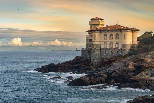 View of Castello del Boccale perched on a rugged rocky cliff overlooking the Tyrrhenian Sea under a soft sunset sky with scattered clouds Livorno Tuscany Italy. View of Castello del Boccale perched on a rugged rocky cliff overlooking the Tyrrhenian Sea under a soft sunset sky with scattered clouds Livorno Tuscany Italy.