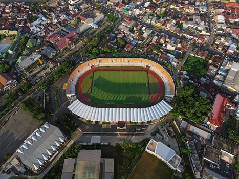 Aerial view of Segiri Stadium featuring a green pitch red running track and white roof structure surrounded by the dense urban landscape of Samarinda East Kalimantan Indonesia. Aerial view of Segiri Stadium featuring a green pitch red running track and white roof structure surrounded by the dense urban landscape of Samarinda East Kalimantan Indonesia.
