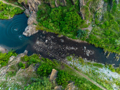 Aerial view of a river flowing through a rocky landscape with lush green vegetation and people swimming in a natural pool in Udaipur Rajasthan India.