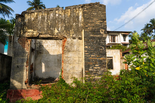 View of an abandoned ruined stone building overgrown with lush green vegetation under a clear sky in Galle Southern Province Sri Lanka.