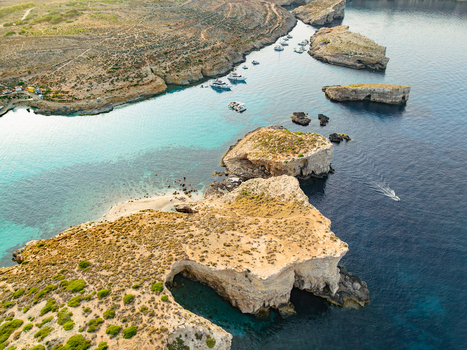 Aerial view of turquoise waters meet rugged cliffs and boats dotting the horizon at Blue Lagoon Comino Malta. Aerial view of turquoise waters meet rugged cliffs and boats dotting the horizon at Blue Lagoon Comino Malta.