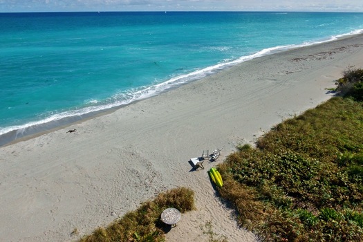 Aerial view of the turquoise ocean meeting the sandy beach contrasting with the green vegetation Jupiter Island Florida United States.