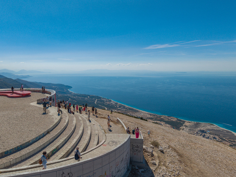 Aerial view of the Bregdet.al Llogara Pass viewing platform with people standing on the curved concrete structure overlooking the Ionian Sea coastline in Llogara Vlore County Albania. Aerial view of the Bregdet.al Llogara Pass viewing platform with people standing on the curved concrete structure overlooking the Ionian Sea coastline in Llogara Vlore County Albania.