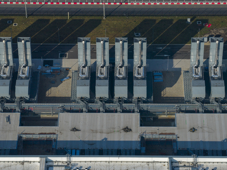 Aerial view of an AI data center with cooling towers and cloud computing hub exterior featuring industrial exhaust stacks and long shadows on the ground. Aerial view of an AI data center with cooling towers and cloud computing hub exterior featuring industrial exhaust stacks and long shadows on the ground.
