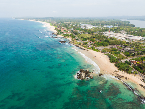 Aerial view of turquoise ocean waves crashing on a sandy beach with coastal buildings and lush tropical greenery Koggala Southern Province Sri Lanka. Aerial view of turquoise ocean waves crashing on a sandy beach with coastal buildings and lush tropical greenery Koggala Southern Province Sri Lanka.