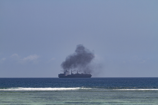 View of a large cargo ship emitting thick black smoke on the horizon from Tiwi Beach Tiwi Wilaya ya Kwale Kenya. View of a large cargo ship emitting thick black smoke on the horizon from Tiwi Beach Tiwi Wilaya ya Kwale Kenya.