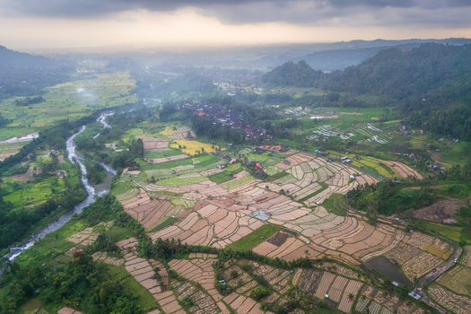 Aerial view of the lush Sidemen rice terraces and a winding river flowing through the tropical valley under a cloudy sky in Sidemen Bali Indonesia.