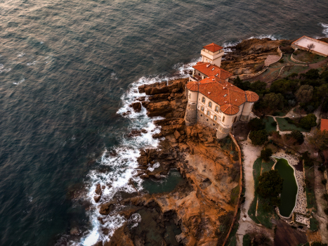 Aerial view of the historic Castello del Boccale perched on rocky cliffs with waves crashing against the shore during sunset in Calafuria Toscana Italy.