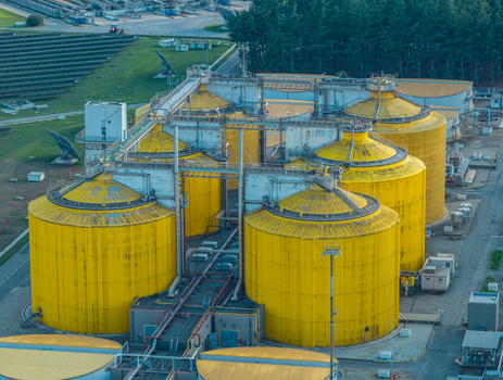 Aerial view of large yellow anaerobic digestion tanks used for biogas production and sewage sludge treatment at an industrial facility in Italy.