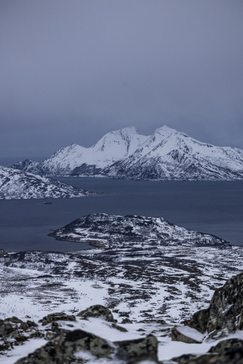 View of snow covered mountain peaks and dark fjord waters under a moody overcast sky Kvaloya Troms Norway.
