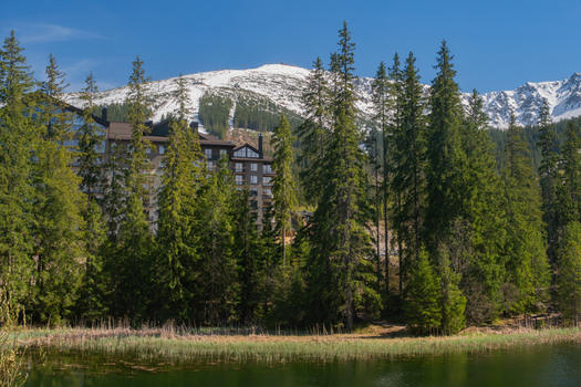 View of Vrbicke pleso lake with dense evergreen forest and a modern hotel with snow capped Low Tatras mountains in the background Demanovska Dolina Zilina Region Slovakia. View of Vrbicke pleso lake with dense evergreen forest and a modern hotel with snow capped Low Tatras mountains in the background Demanovska Dolina Zilina Region Slovakia.