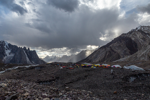 View of the Concordia Campsite nestled among rugged mountain peaks and rocky glacial terrain under a dramatic stormy sky with light rays in Concordia Gilgit Baltistan Pakistan.