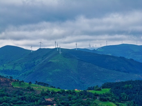 Aerial view of wind turbines standing on lush green mountain ridges under a dramatic cloudy sky in Cudillero Asturias Spain.