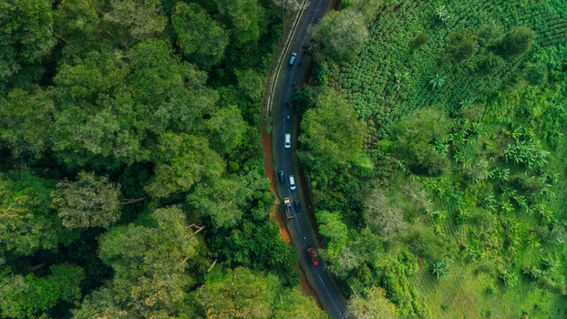 Aerial view of a winding road cutting through dense tropical forest and agricultural fields in Indonesia. Aerial view of a winding road cutting through dense tropical forest and agricultural fields in Indonesia.