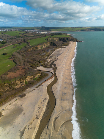 Aerial view of Carlyon Bay featuring a sandy beach a winding stream flowing into the sea coastal cliffs and green fields under a cloudy sky in Carlyon Bay Cornwall United Kingdom. Aerial view of Carlyon Bay featuring a sandy beach a winding stream flowing into the sea coastal cliffs and green fields under a cloudy sky in Carlyon Bay Cornwall United Kingdom.