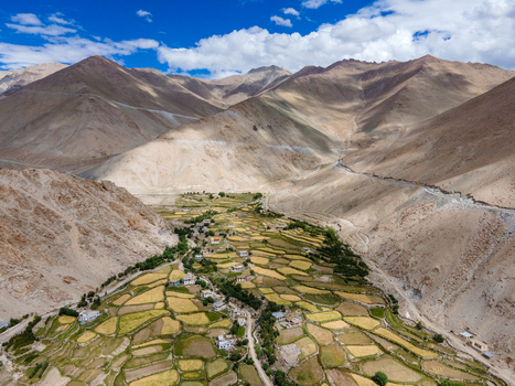 Aerial view of a lush green valley with terraced agricultural fields and small village houses nestled between towering arid mountain ranges in Ladakh India. Aerial view of a lush green valley with terraced agricultural fields and small village houses nestled between towering arid mountain ranges in Ladakh India.