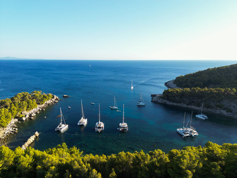 Aerial view of Hvar with sailboats anchored in a clear blue bay surrounded by lush green pine forests and rocky coastline in Split Dalmatia County Croatia.