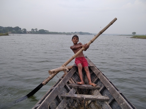 Kushtia Khulna Division Bangladesh 27 April 2020 View of a young boy rowing a wooden boat with a long bamboo pole on a river under an overcast sky. Kushtia Khulna Division Bangladesh 27 April 2020 View of a young boy rowing a wooden boat with a long bamboo pole on a river under an overcast sky.
