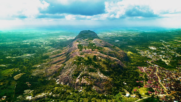 Aerial view of the rugged rocky mountain rising amidst a sea of lush green vegetation casting long shadows under a partly cloudy sky Idanre Nigeria. Aerial view of the rugged rocky mountain rising amidst a sea of lush green vegetation casting long shadows under a partly cloudy sky Idanre Nigeria.