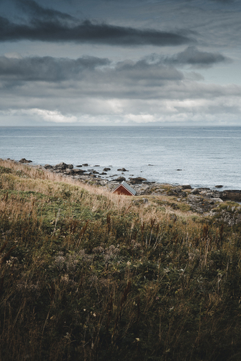 View of Myrland Beach with a small red cabin nestled along the rocky coastline under a dramatic cloudy sky in Napp Nordland Norway. View of Myrland Beach with a small red cabin nestled along the rocky coastline under a dramatic cloudy sky in Napp Nordland Norway.