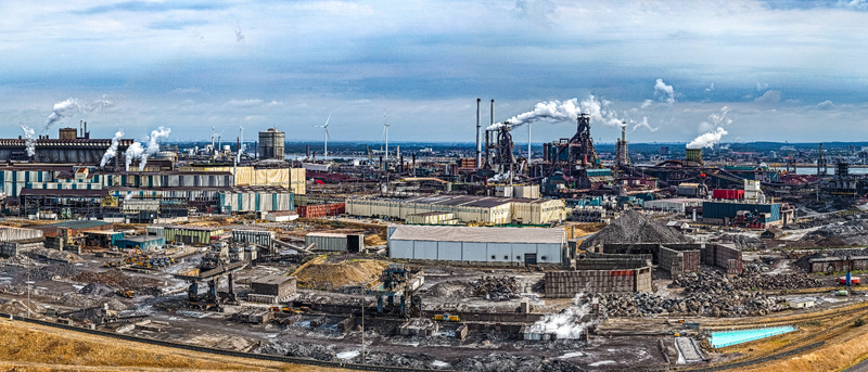 Aerial view of the Tata Steel industrial complex with smoking chimneys large factory buildings and storage yards in Velsen Noord Noord Holland Netherlands. Aerial view of the Tata Steel industrial complex with smoking chimneys large factory buildings and storage yards in Velsen Noord Noord Holland Netherlands.