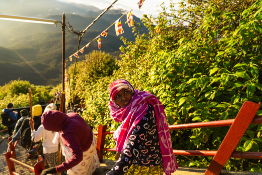 Ratnapura Sri Lanka 23 February 2026 View of pilgrims climbing the stairs of Adam s Peak with Buddhist flags and lush green mountains under golden sunlight.