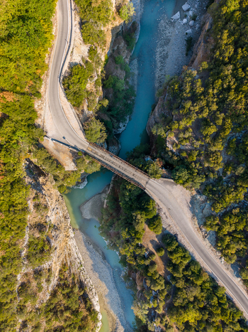 Aerial view of Osumi canyon with a bridge crossing the turquoise river surrounded by steep rocky cliffs and lush green trees in Dhores Berat County Albania.