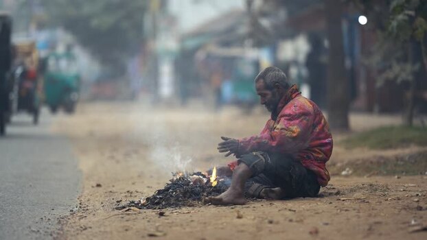 View of a man warming himself by a fire on a misty road Bangladesh. View of a man warming himself by a fire on a misty road Bangladesh.