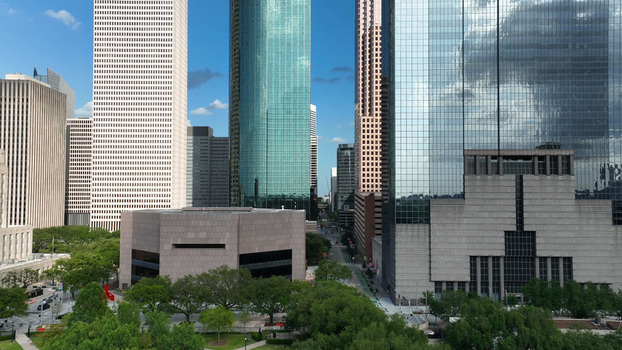 Aerial view of the Houston skyline featuring modern glass skyscrapers urban architecture and lush green trees under a clear blue sky in Harris County Texas United States.
